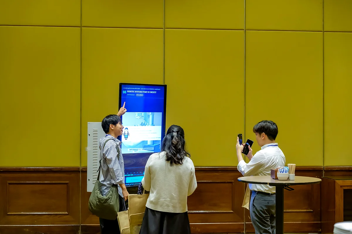 ผู้ร่วมงานแตะเลือกดูผลงานและถ่ายรูปหน้าจอ E-Poster ในงานประชุมวิชาการ