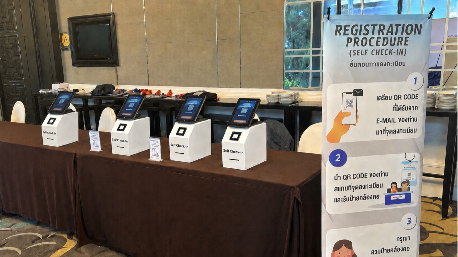 ภาพถ่ายจริงจากงาน — เครื่อง Self Check-in 4 เครื่องพร้อม Registration Procedure banner ที่จัดโดย MeetingThai